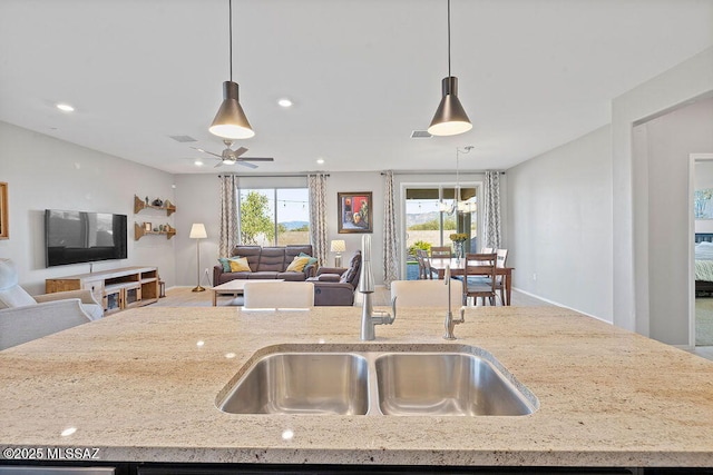 kitchen featuring ceiling fan, sink, pendant lighting, and light stone counters