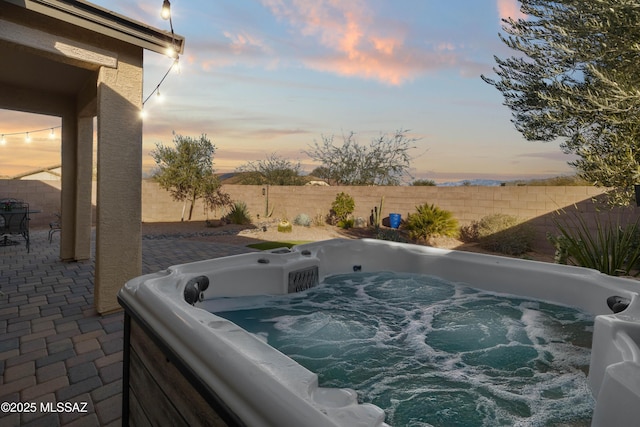 pool at dusk featuring a patio area and a hot tub