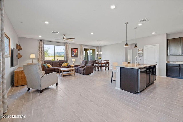 kitchen featuring sink, hanging light fixtures, dark brown cabinets, dishwasher, and a kitchen island with sink