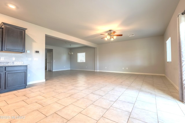 unfurnished room with light tile patterned flooring, a wealth of natural light, and ceiling fan with notable chandelier