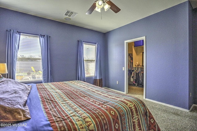 carpeted bedroom with a walk in closet and ceiling fan