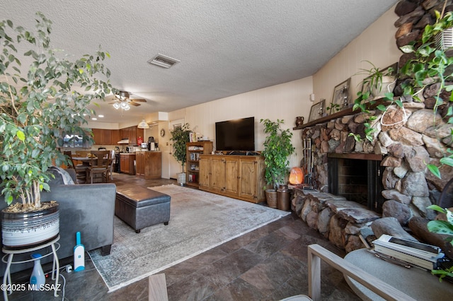 living room featuring a textured ceiling, ceiling fan, and a fireplace