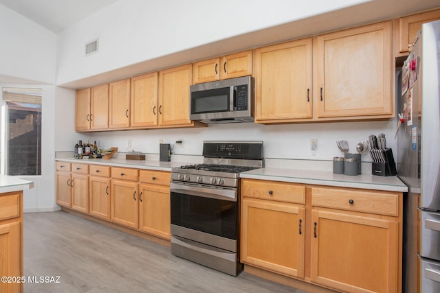 kitchen with stainless steel appliances, light brown cabinetry, and light hardwood / wood-style flooring