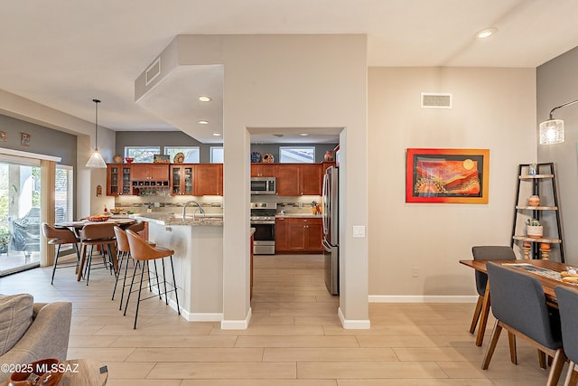 kitchen featuring pendant lighting, light hardwood / wood-style flooring, appliances with stainless steel finishes, a kitchen breakfast bar, and light stone countertops