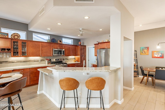 kitchen featuring a breakfast bar area, light hardwood / wood-style flooring, ceiling fan, stainless steel appliances, and light stone countertops