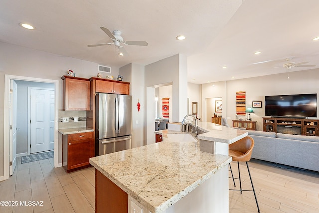 kitchen with stainless steel fridge, a kitchen breakfast bar, light hardwood / wood-style floors, light stone countertops, and an island with sink