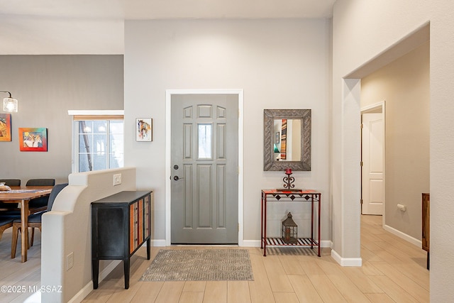 foyer entrance with a towering ceiling, a healthy amount of sunlight, and light wood-type flooring