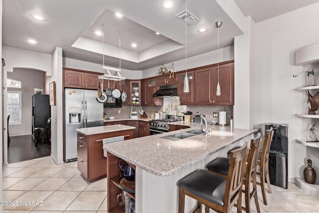 kitchen featuring appliances with stainless steel finishes, a breakfast bar, kitchen peninsula, sink, and a tray ceiling