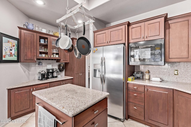 kitchen with tasteful backsplash, black microwave, light tile patterned floors, stainless steel fridge with ice dispenser, and light stone countertops