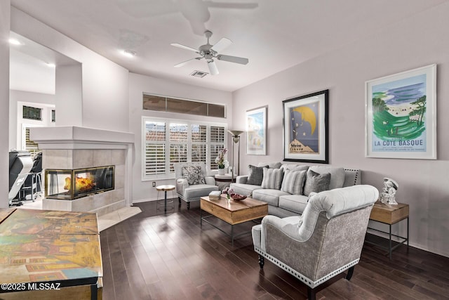 living room featuring dark wood-type flooring, ceiling fan, and a tile fireplace