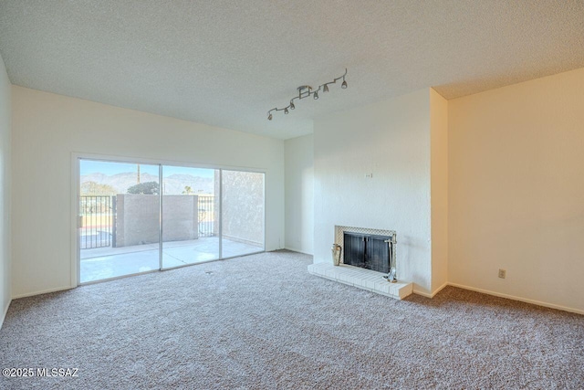 unfurnished living room with rail lighting, a brick fireplace, carpet flooring, and a textured ceiling