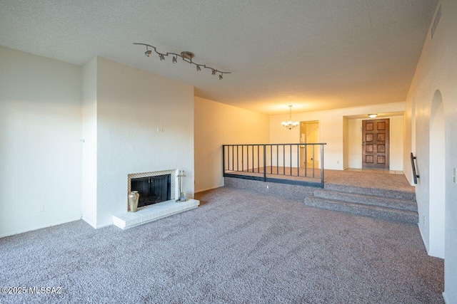 unfurnished living room featuring rail lighting, a chandelier, a brick fireplace, a textured ceiling, and carpet flooring