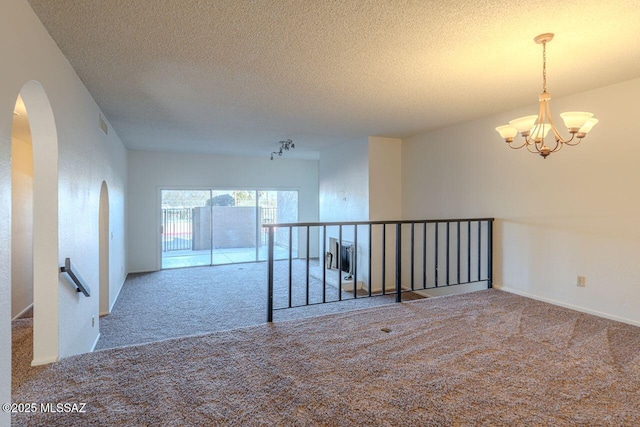 spare room with an inviting chandelier, light colored carpet, and a textured ceiling