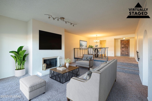 carpeted living room featuring a tiled fireplace, rail lighting, an inviting chandelier, and a textured ceiling