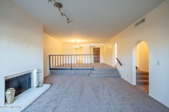 unfurnished living room with track lighting, a chandelier, dark carpet, and a textured ceiling