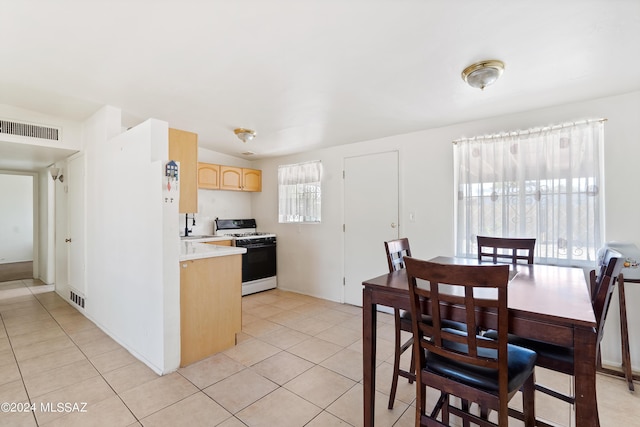 kitchen featuring light tile patterned floors, light brown cabinets, white gas range oven, and sink