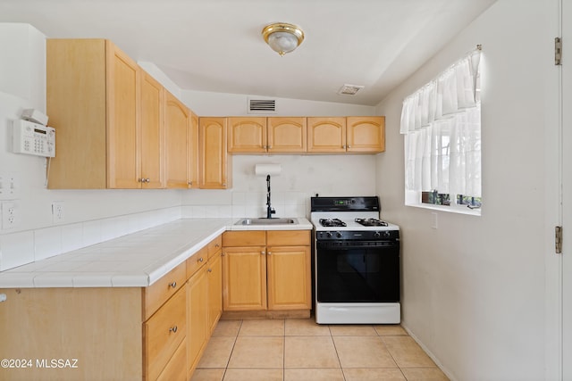 kitchen featuring gas stove, light brown cabinets, sink, tile countertops, and light tile patterned floors