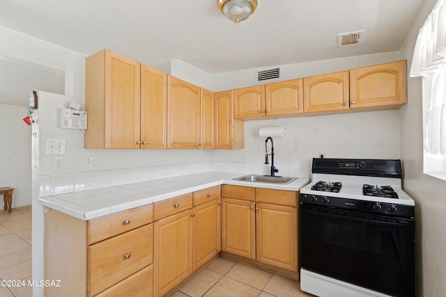 kitchen featuring tile counters, sink, range with gas stovetop, and light brown cabinetry