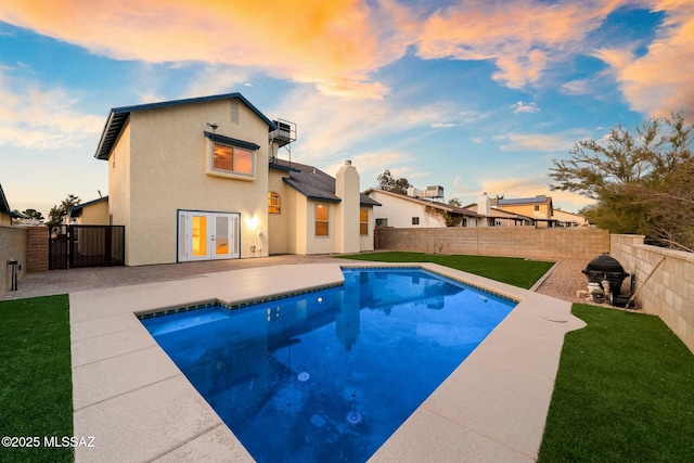 pool at dusk featuring french doors, a patio area, and a lawn