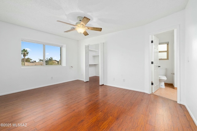 unfurnished bedroom with hardwood / wood-style flooring, ensuite bathroom, a walk in closet, and ceiling fan