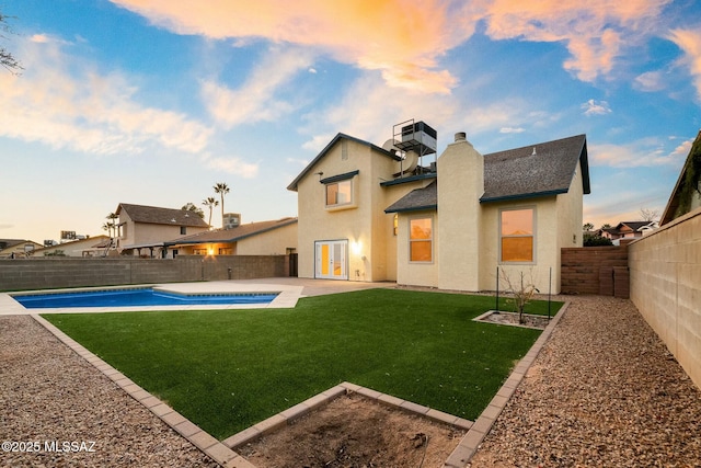 back house at dusk with a fenced in pool, a patio, and a yard