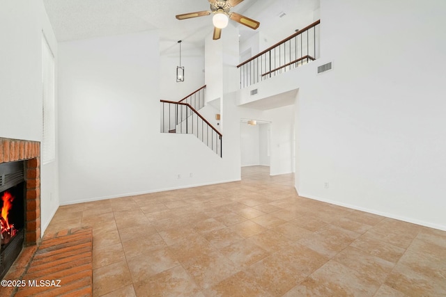 unfurnished living room featuring a textured ceiling, a fireplace, ceiling fan, and a high ceiling