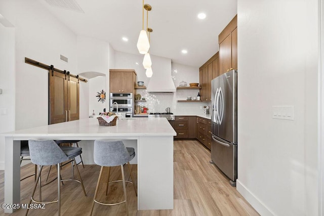 kitchen with appliances with stainless steel finishes, pendant lighting, backsplash, a barn door, and custom range hood