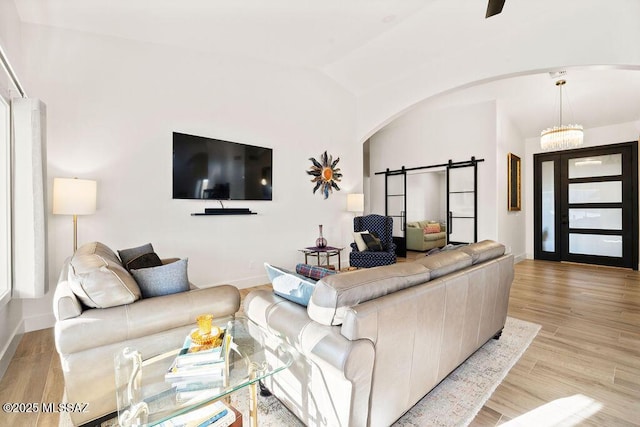 living room featuring an inviting chandelier, light hardwood / wood-style flooring, a barn door, and vaulted ceiling