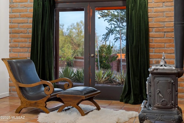 living area featuring light tile patterned flooring, brick wall, and a wood stove