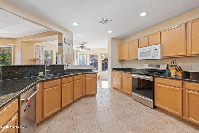 kitchen featuring appliances with stainless steel finishes, sink, dark stone counters, light tile patterned floors, and ceiling fan