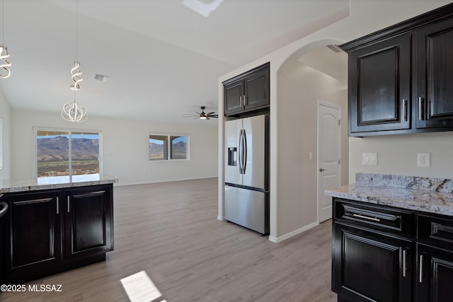 kitchen featuring stainless steel refrigerator with ice dispenser, ceiling fan, hanging light fixtures, light stone counters, and light hardwood / wood-style flooring