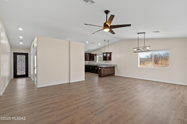 unfurnished living room featuring light hardwood / wood-style floors, sink, vaulted ceiling, and ceiling fan with notable chandelier