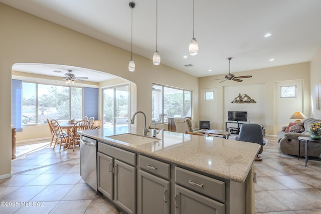 kitchen with dishwasher, hanging light fixtures, sink, light stone countertops, and a center island with sink