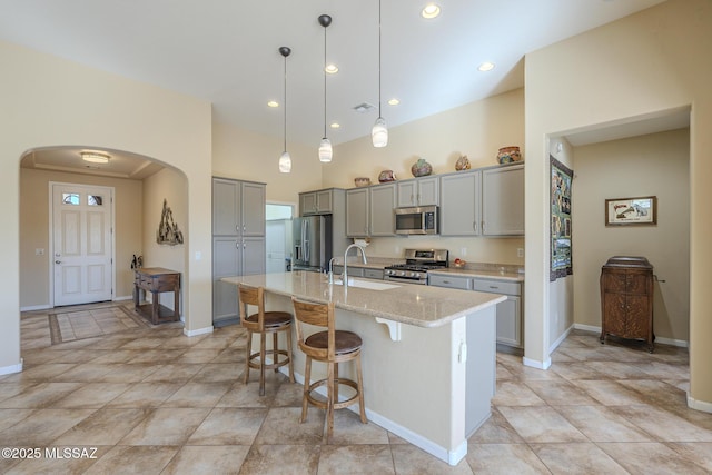 kitchen featuring light stone countertops, stainless steel appliances, sink, a kitchen island with sink, and gray cabinetry