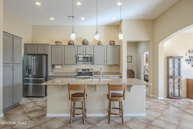 kitchen featuring pendant lighting, light stone countertops, a kitchen bar, an island with sink, and stainless steel appliances