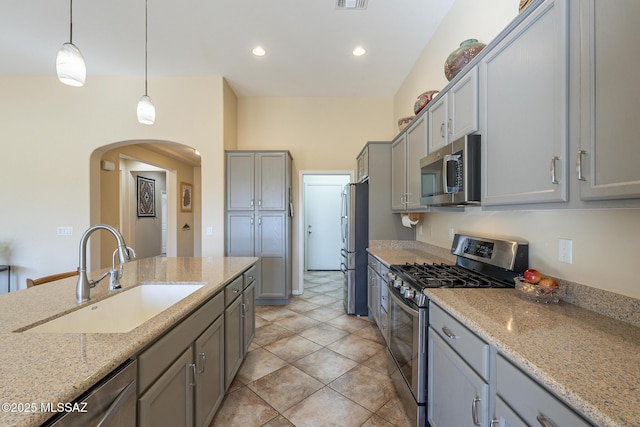 kitchen with hanging light fixtures, appliances with stainless steel finishes, sink, gray cabinetry, and light stone countertops