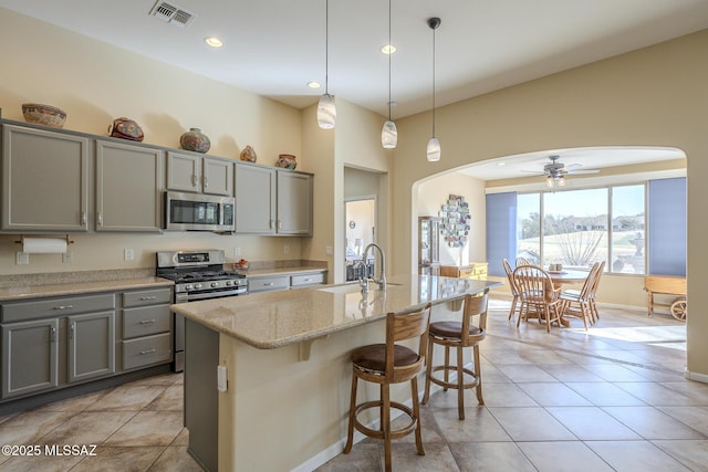 kitchen with sink, stainless steel appliances, light stone counters, a center island with sink, and gray cabinets