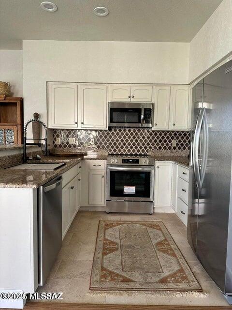 kitchen with stainless steel appliances, dark stone countertops, white cabinets, and sink