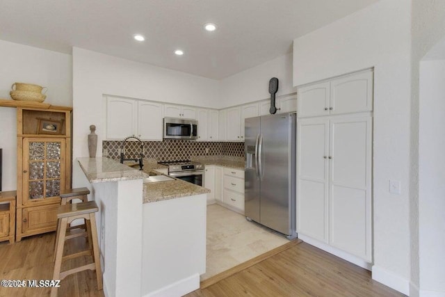 kitchen with tasteful backsplash, kitchen peninsula, a kitchen bar, stainless steel appliances, and white cabinets