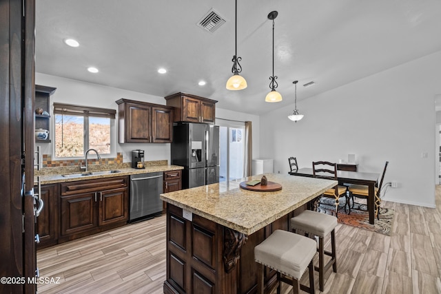 kitchen with a center island, appliances with stainless steel finishes, light stone countertops, hanging light fixtures, and dark brown cabinets