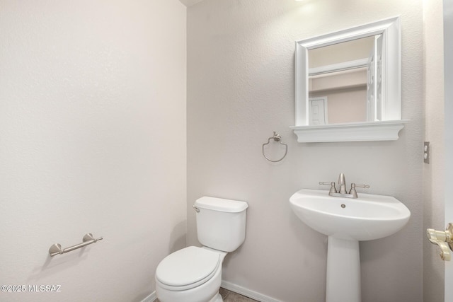 half bathroom featuring toilet, baseboards, and a sink