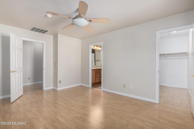 unfurnished bedroom with a walk in closet, a closet, ceiling fan, and light wood-type flooring