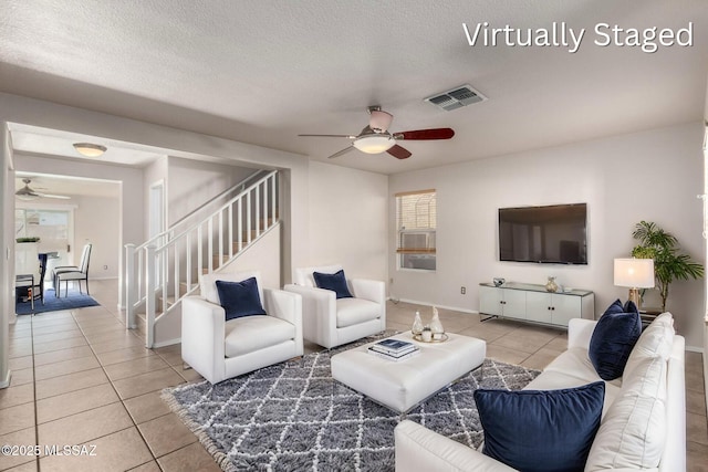 living area featuring light tile patterned floors, visible vents, a textured ceiling, and stairs