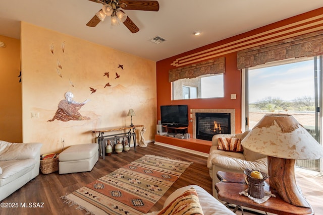 living room with a tiled fireplace, wood-type flooring, and ceiling fan