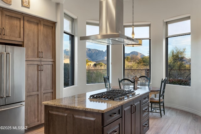 kitchen with appliances with stainless steel finishes, a center island, light stone counters, island range hood, and a mountain view