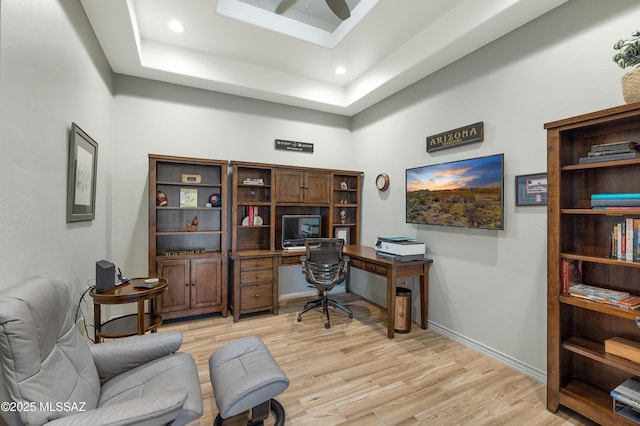 office space with a raised ceiling, ceiling fan, and light hardwood / wood-style floors