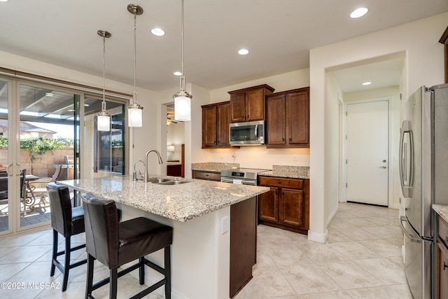 kitchen featuring an island with sink, stainless steel appliances, light stone countertops, and sink