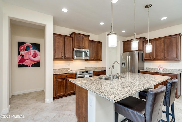 kitchen with decorative light fixtures, sink, a kitchen island with sink, stainless steel appliances, and light stone countertops