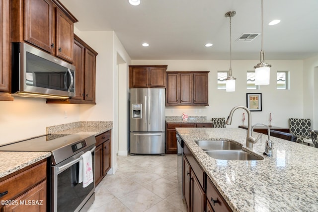 kitchen featuring light stone counters, sink, decorative light fixtures, and stainless steel appliances