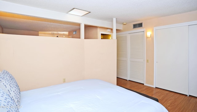 bedroom with two closets, wood-type flooring, and a textured ceiling